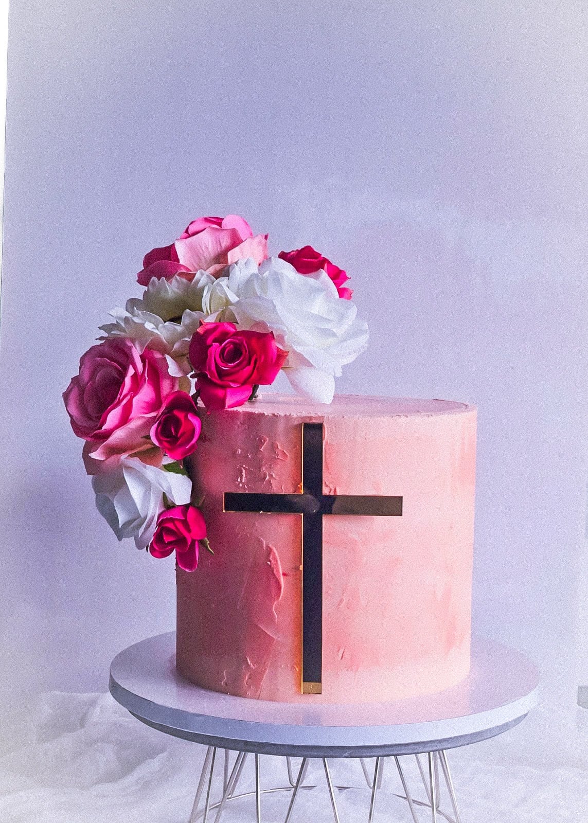 Blush pink cake with a gold cross and fresh roses