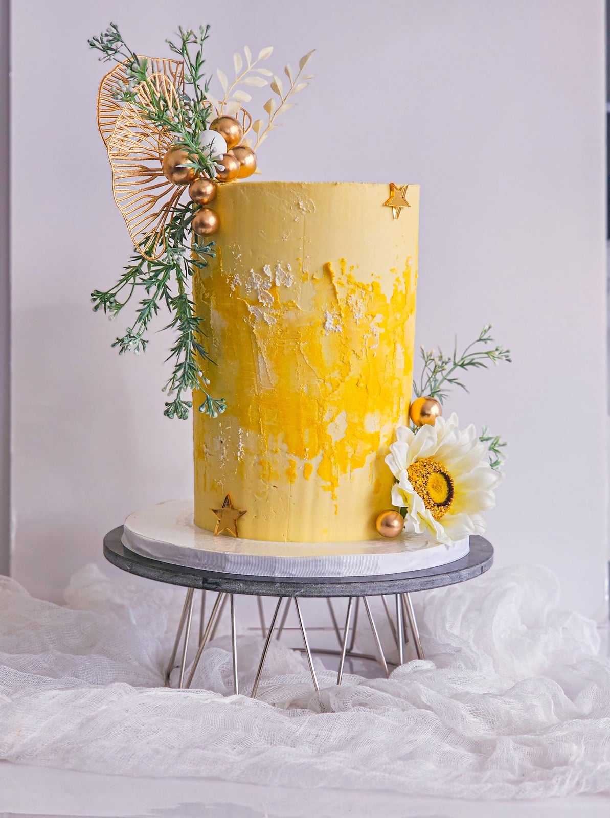 Tall yellow buttercream cake with gold leaf, dried florals and pearls