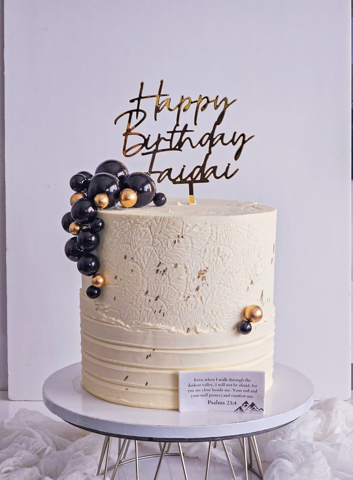 Textured ivory buttercream cake with dark spheres and a script topper